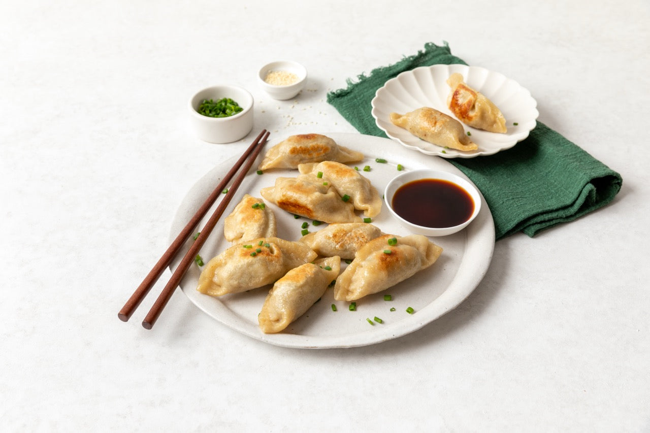 FroPro High protein dumplings on a plate with soy sauce, green onions, and chopsticks on a white background
