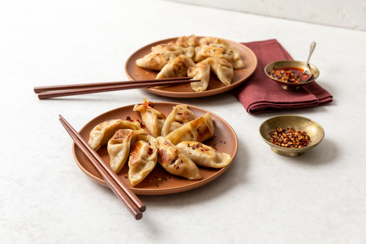 Two plates of FroPro high protein dumplings with chopsticks and small bowls on a white surface